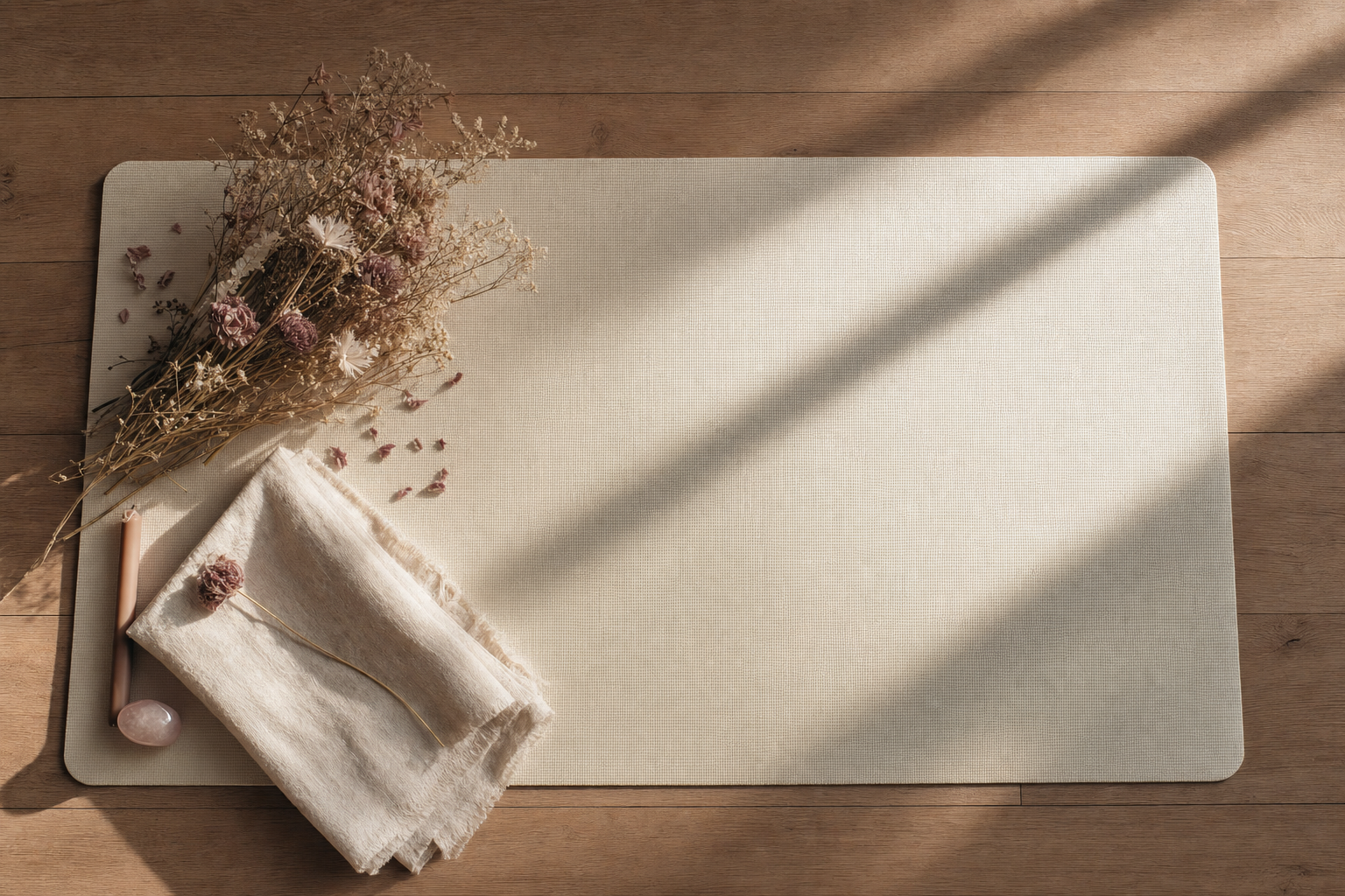 An overhead view of a cream yoga mat with dried flowers and a folded linen blanket in warm afternoon light