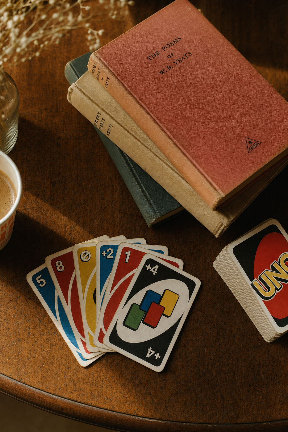 A fanned hand of Uno cards on a worn wooden library table beside a stack of hardcover books and a coffee cup